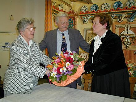 Kreisgruppe Bad Tlz/Wolfratshausen: Vor dem Hintergrund der Bauernstuben-Kulisse berreicht Chorsprecherin Rose-May Schibschid einen Blumenstrau an Kunigunde Fischer (rechts) vor den Augen des Bruders Wilhelm Bretz aus Amerika.